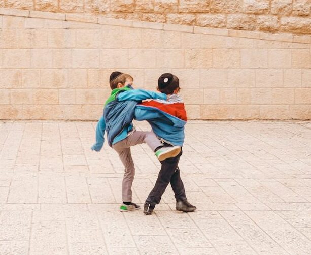 2 boys in green and blue jacket walking on gray concrete floor during daytime